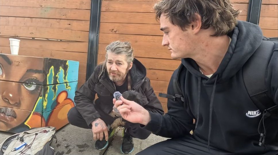 Nick Shirley interviews a man beside a wooden wall in Kensington, Philadelphia.